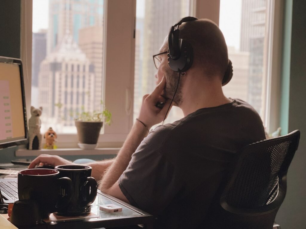 Top 7 High-Paying Remote Jobs You Can Actually Land in 2026 A man wearing headphones works at his desk overlooking a city skyline from a home office.
