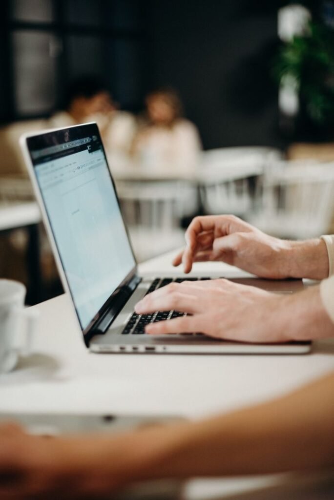 Is Job Hopping Really Bad for Your Career? Close-up of hands typing on a laptop in a cozy indoor cafe setting.