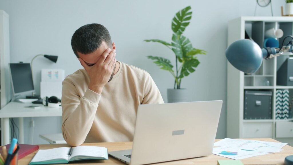 5 Signs It Might Be Time to Change Careers Young man overwhelmed at his desk with laptop, office stress.