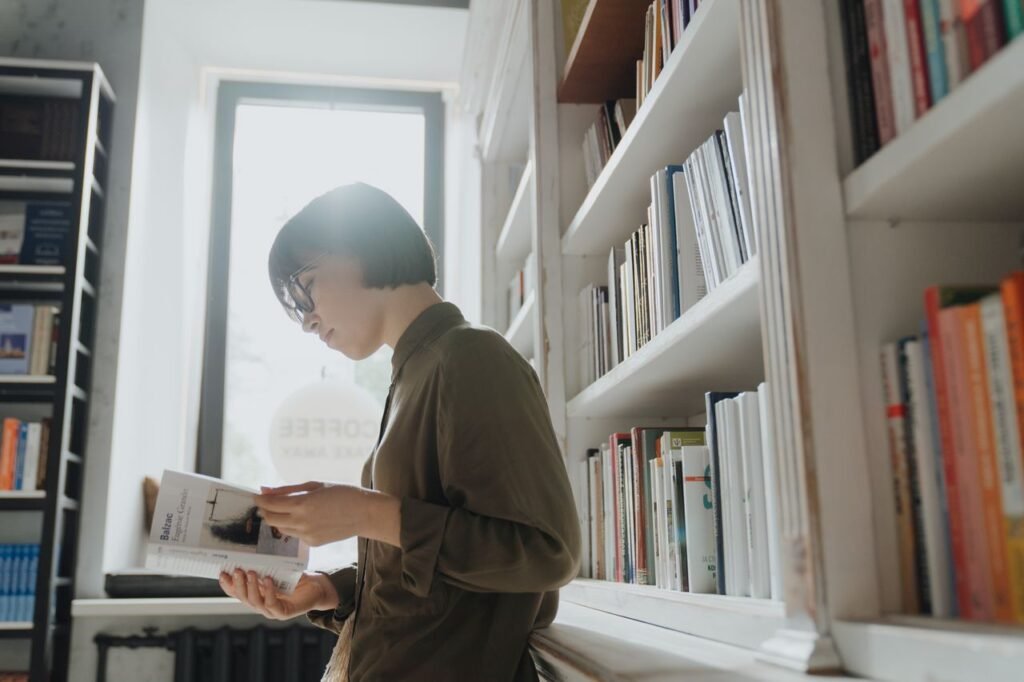 A woman in glasses reading a book in a modern library setting, emphasizing learning and leisure.