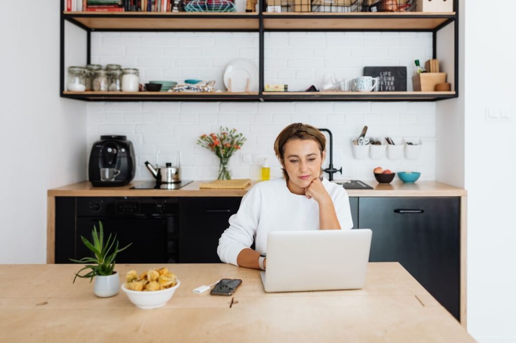 Adult woman focused on laptop work in a modern kitchen setting.