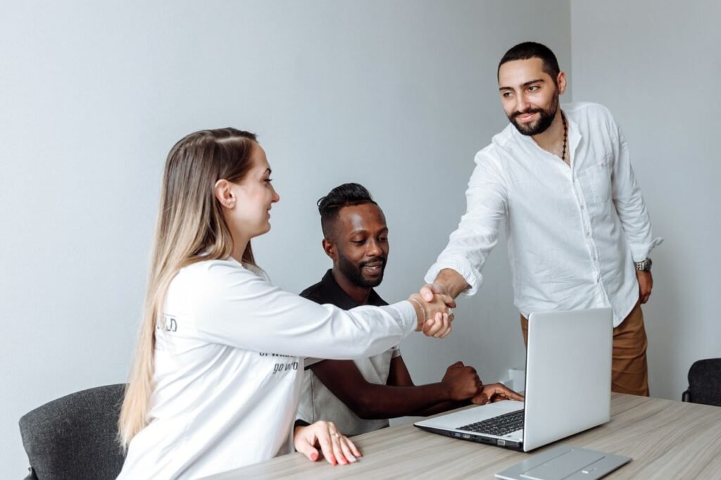 Diverse team members shaking hands over a desk in a modern office setting.