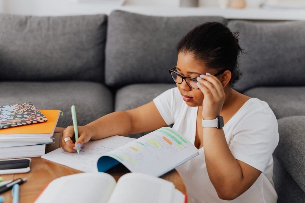 How Long Does It Take to Land Your First Nursing Job After Getting Your RN License? A young woman wearing glasses studies with a notebook on a table indoors, highlighting focus and learning.