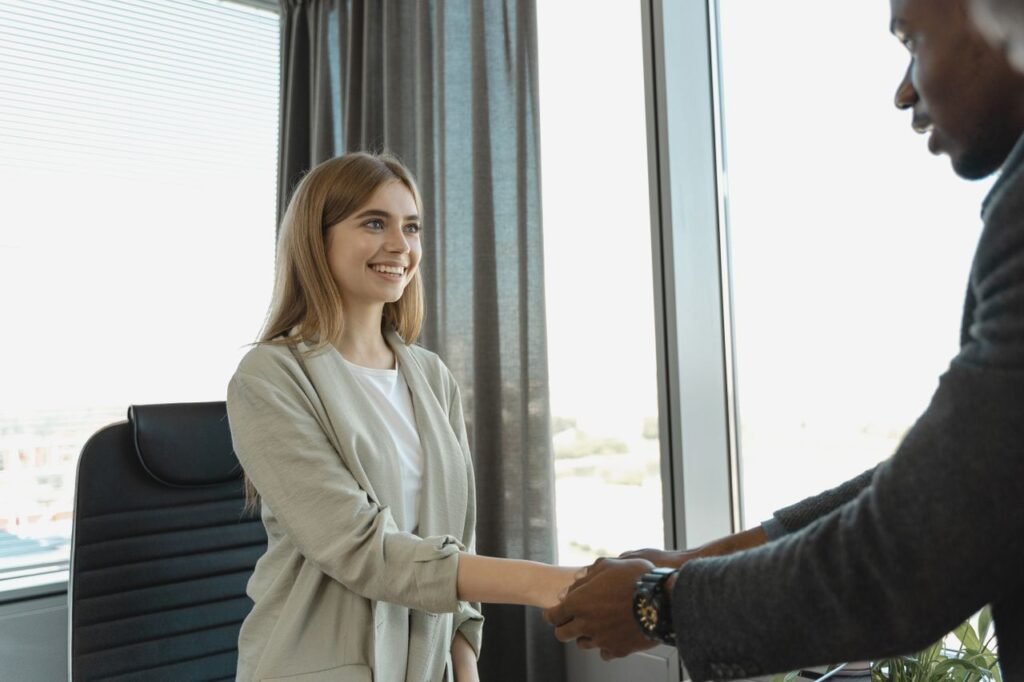 Busting the Myth: Do You Really Need a College Degree to Get Hired? Woman smiling and shaking hands at a business office, signaling a successful job interview.