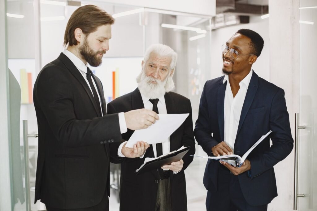 Government Jobs vs Private Sector: Which One Actually Wins? Three businessmen in suits discussing documents in a modern office setting, engaging in teamwork.
