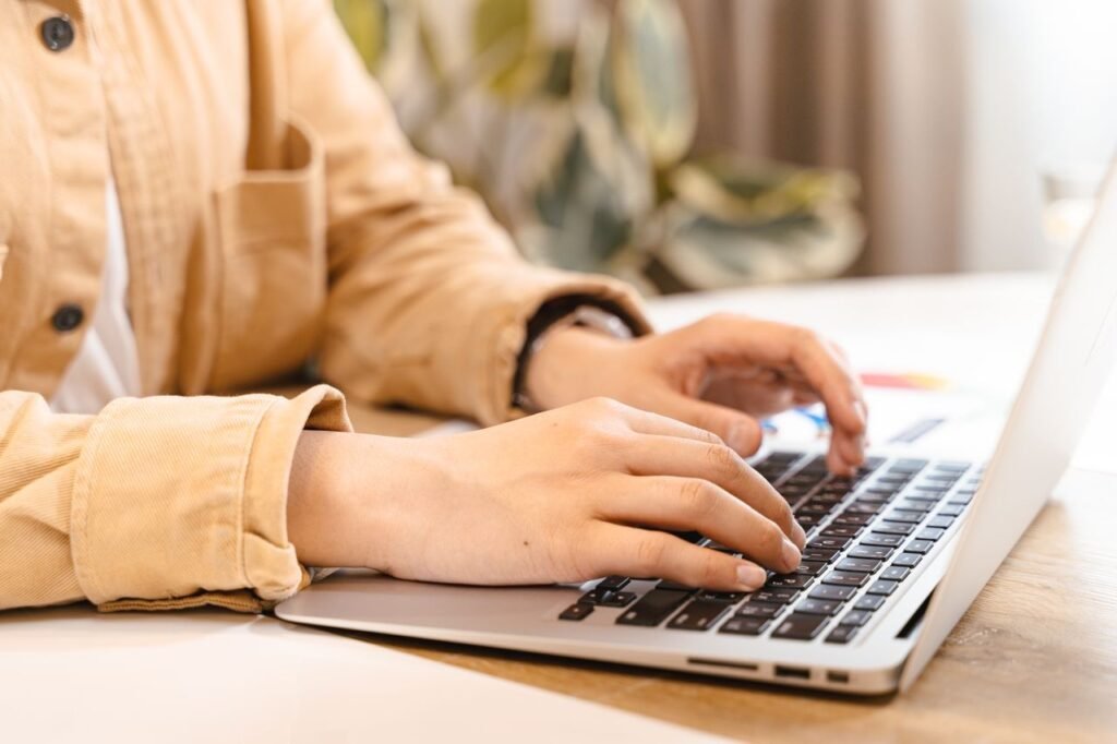 Do You Really Need a Cover Letter in the US Job Market? Close-up of hands typing on a laptop in a bright indoor setting, emphasizing work and technology.