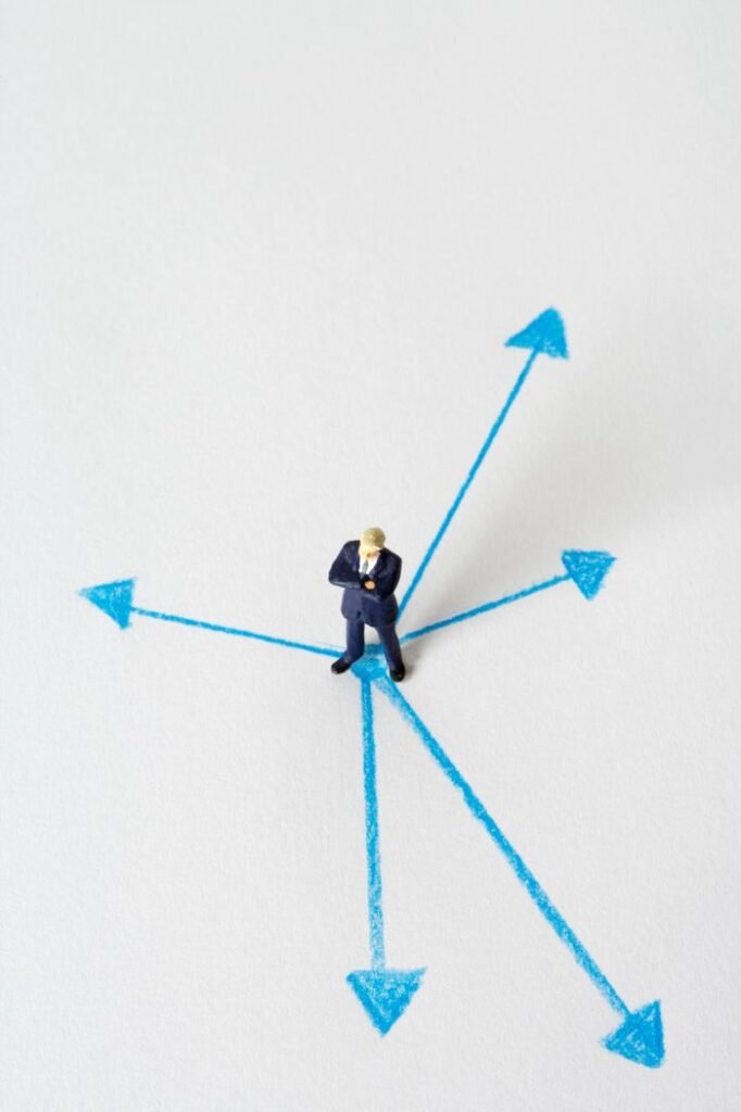 Job Security vs Career Growth: Which Should You Prioritize? Miniature businessman stands at crossroads of blue arrows on white background, symbolizing choices.