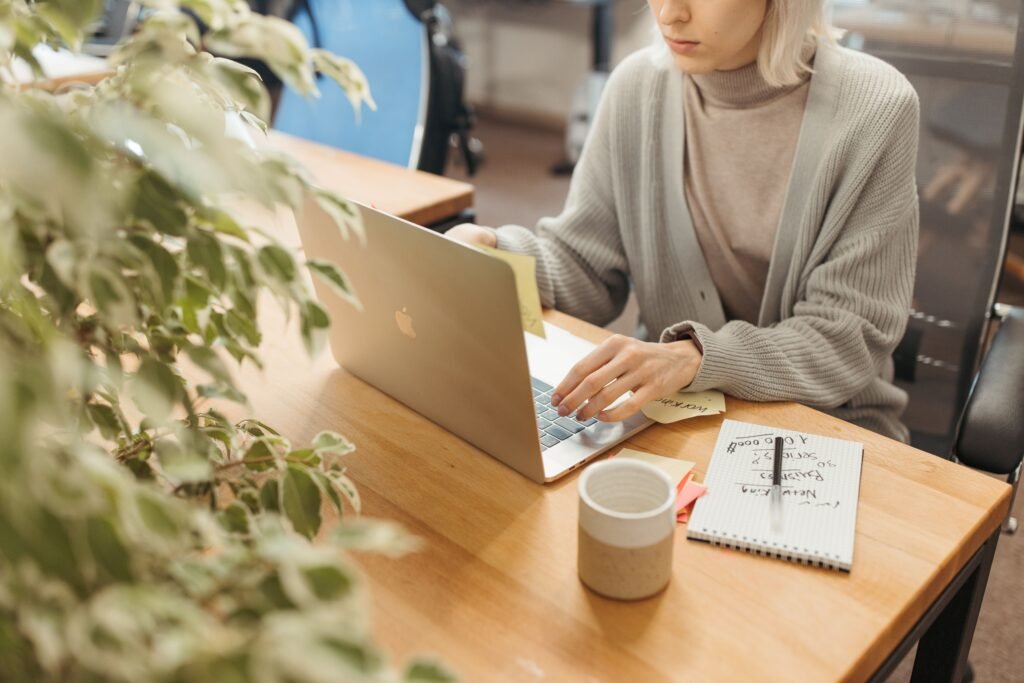 How to Write a Thank You Email After a Job Interview: A Step by Step Guide A woman working on a laptop at a wooden desk in a bright, modern office setting.