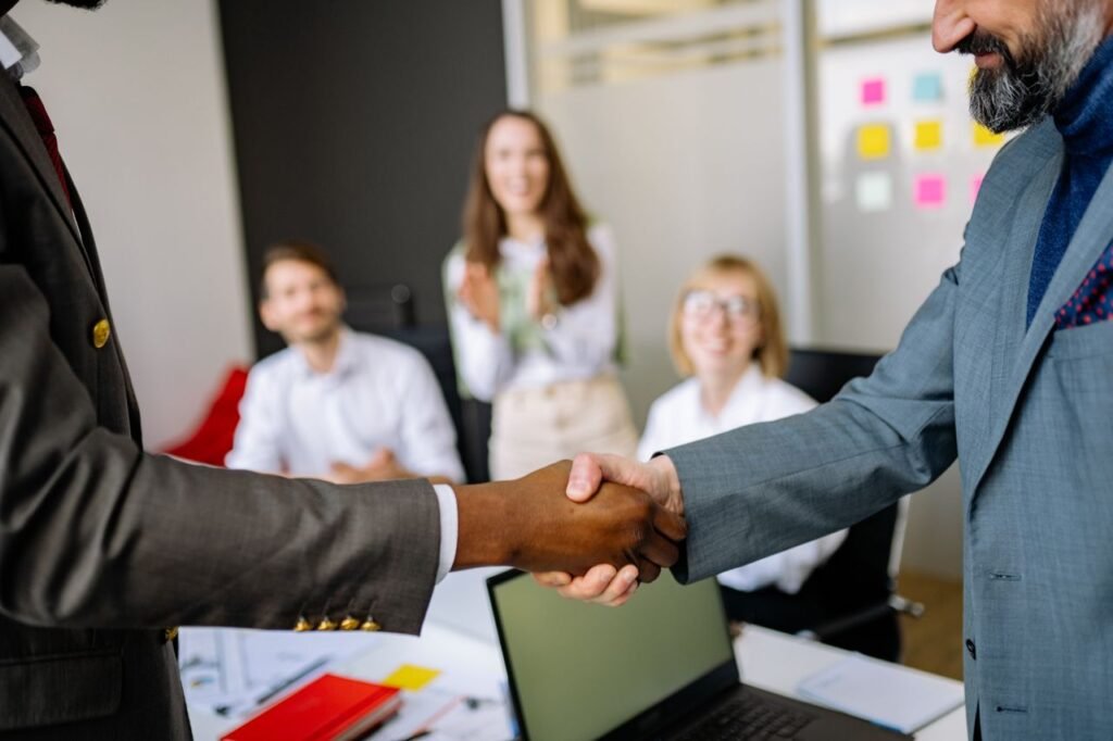 How to Ask for a Promotion (Without Feeling Awkward About It) Close-up of a handshake between colleagues in a professional office setting, emphasizing teamwork and agreement.